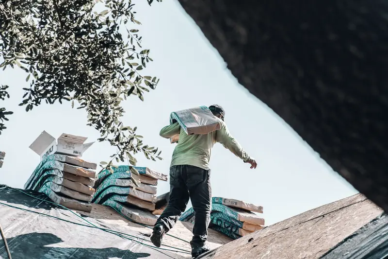 Roofer carrying a bundle of shingles across a residential roof